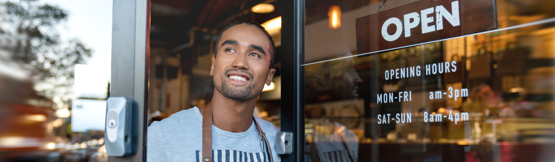 man smiling opening the doors of a cafe with an open sign displayed in window